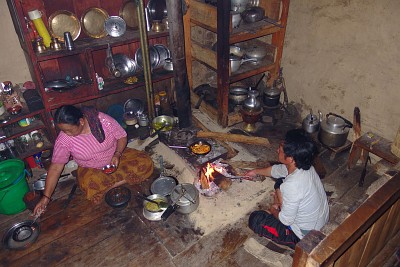 Day 15: the kitchen in our lodge. The lady is preparing our dhal bhat, Santosh is tending the fire. Note the pressure cooker near the fire containing the rice, the pans with the curries on the stove, a mortar in front of her for preparing a tomato sauce, the dhal is in the pot with the lid on. The water kettle, essential in a Nepali kitchen is not needed at the moment and is on the left against the wall.